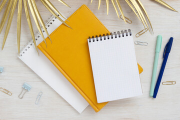 Different notebooks pens paper clips stationery on  table top view. Summer concept with palm leaves mocap for lettering