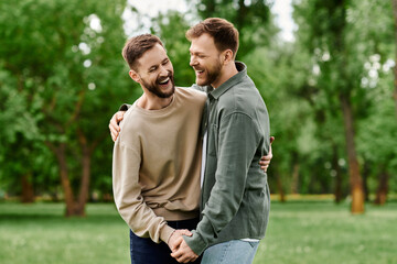 Two bearded men, in a loving embrace, laugh together in a green park.