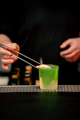 close-up of beautiful crystal glass with green alcoholic drink which man decorates with apple