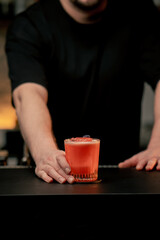 Bartender holding glass filled with fresh orange cocktail with sour and sweet taste