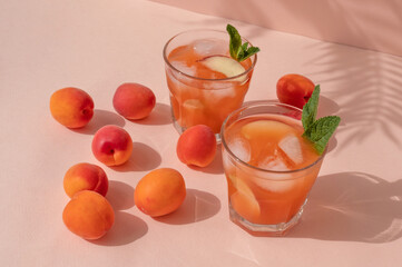 Peaches and apricots, glasses with fruit iced refreshing summer drinks on bright pink background in sun light