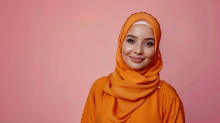 Young smiling beautiful arabian asian muslim woman wear orange abaya hijab look camera isolated on plain light pink color background studio portrait. People uae middle eastern islam religious concept.