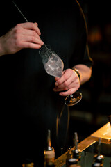 A professional bartender stirs an ice-cold cocktail in a beautiful ornate glass on a bar counter on a blurred background