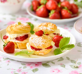 Cream puffs cakes or profiterole filled with whipped cream served with strawberries