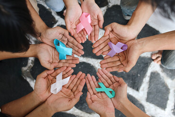 World cancer day. Hands of people open and holding colourful awareness ribbons forming circle as...