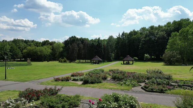 Bowers in park during a beautiful summer day surrounded by lush greenery, grass, flowers and trees under a clear blue sky