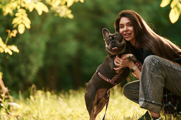 Sitting on the grass, embracing an animal. Young pretty woman is with her dog in the park