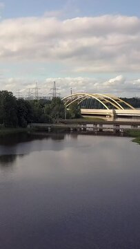 Flying over beautiful landscape a large automobile bridge over the lake, forest. Beautiful reflection in the water. Aerial view. Vertical shot.