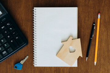 Blank notebook, calculator and model of a house on a wooden table, flat lay.