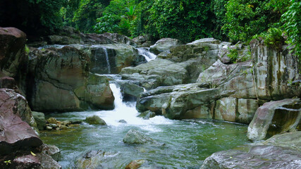 Mountain river in a tropical rainforest. The bed of a mountain river flows over the rocks, forming a cascading waterfall in the jungle.