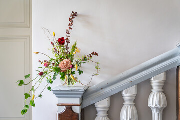Interior design with bouquet spring flowers and glamelia in vase on wooden stair column. Spring...