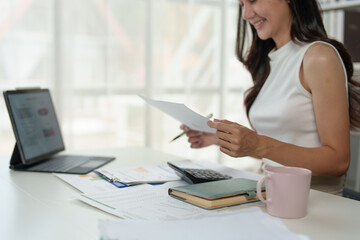 Fototapeta premium Attractive Asian businesswoman sitting on laptop computer and financial documents Home office planning is preparing internal audit document balance calculation report.