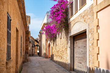 Fototapeta premium Alcudia, Majorca old town with beautiful flowers hanging down a building, horizontal shot during dusk, Mallorca