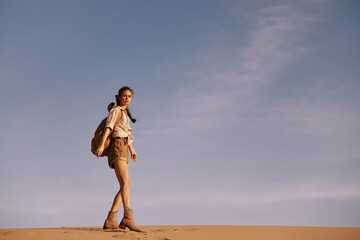 Solitary woman trekking across desert sand dune with bag under blue sky, isolated adventure journey...