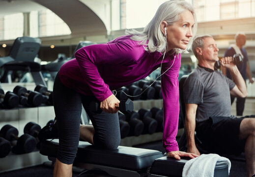 Dumbbell, fitness and music with mature woman on bench in gym for physical training or workout. Exercise, health and wellness with confident athlete person in performance club for active challenge