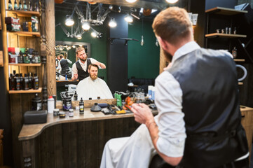 Hairdresser making final touches in new haircut. Comfortable atmosphere in modern barbershop.