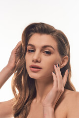 Fototapeta premium A young woman with long wavy hair gently touches her face.