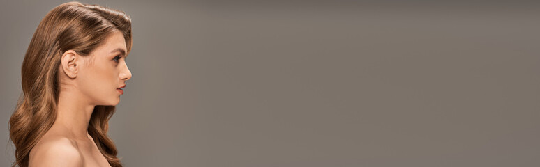 A young beautiful woman with long wavy hair stands gracefully against a gray background, banner.