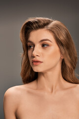 Fototapeta premium A young woman with long wavy hair strikes a pose on gray backdrop, exuding confidence and elegance.