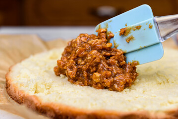Putting caramel and nuts filling on a biscuit with spoon