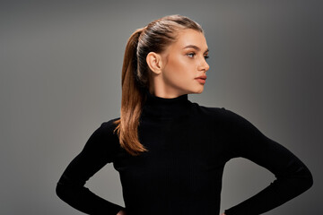A young beautiful woman with long wavy hair, standing with hands on hips in a confident and poised...