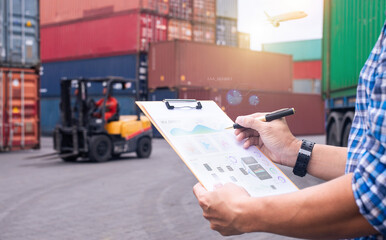 Logistics manager reviewing documents at a shipping yard, with a forklift and cargo containers in...