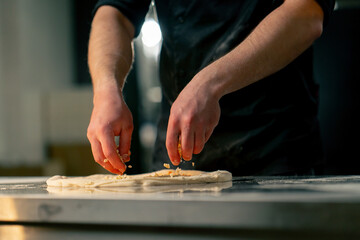 close up in a professional kitchen in a pizzeria young chef in a black uniform puts ingredients on pizza