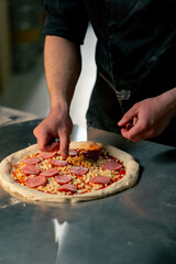 close up in a professional kitchen in a pizzeria young chef in a black uniform puts ingredients on pizza