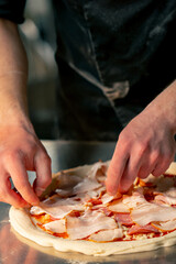 close up in a professional kitchen in a pizzeria young chef in a black uniform puts ingredients on pizza