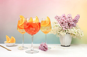 Festive alcoholic cocktail Aperol spritz in glasses on a bright background with a bouquet of...