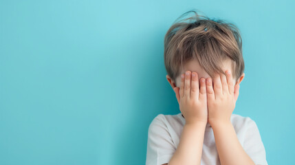 Boy covering face with hands on color background