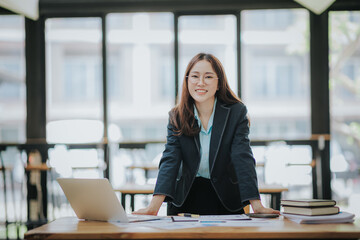 Young Asian professional business woman office worker analyst sitting at desk working on laptop thinking on project plan, analyzing marketing or financial data online, watching elearning webinar.