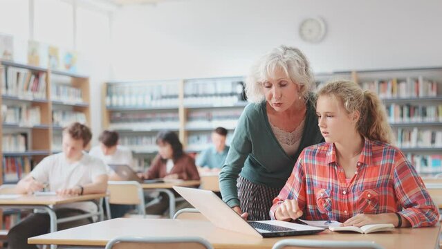 Portrait of adult female librarian and diligent schoolkids during classes in school library