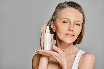 A mature woman in comfy attire holding a spray bottle in her hand, actively posing.