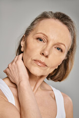 Mature woman in comfy attire striking a graceful pose with hand on neck.