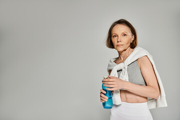 Older woman in comfortable clothing serenely sips from a water bottle.