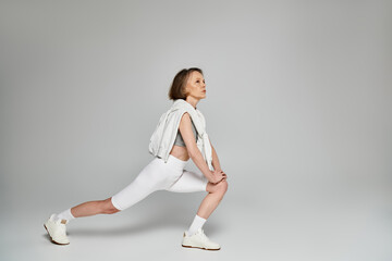 Mature woman in comfortable attire performing a squat on a white background.