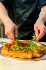 close up in a professional kitchen in a pizzeria young chef in a black uniform puts ingredients on pizza