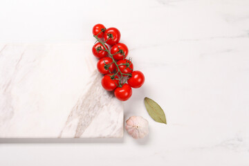 Cutting board, garlic, bay leaf and tomatoes on white marble table, flat lay. Space for text