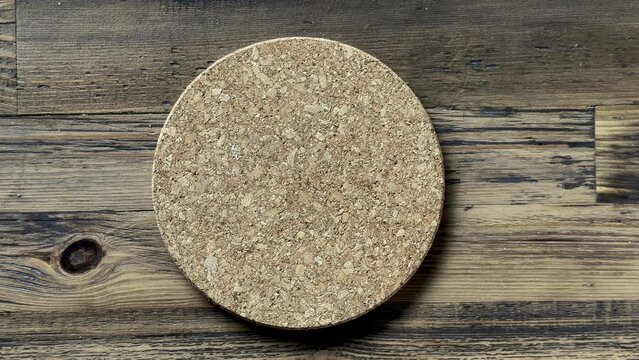 cook puts round cork mat on kitchen wooden table to protect it from heat, top view