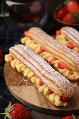 Delicious eclairs filled with cream and strawberries on table, closeup