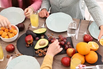 Friends eating vegetarian food at wooden table indoors, closeup