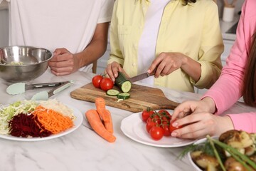 Friends cooking healthy vegetarian meal at white marble table in kitchen, closeup