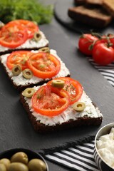 Delicious ricotta bruschettas with sliced tomatoes, olives and greens on black table, closeup
