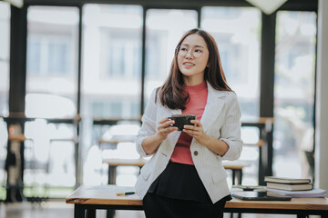 Beautiful Asian businesswoman holds a coffee cup and is drinking coffee in the morning before...