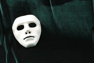 Theater arts. White mask on green fabric, top view. Space for text
