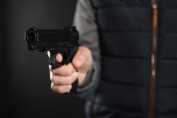 Dangerous criminal with gun on black background, closeup. Armed robbery
