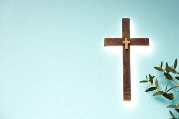 Shining cross and eucalyptus branches on turquoise background, space for text. Religion of...