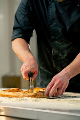 close up in a professional kitchen in pizzeria the chef cuts the pizza into pieces with a round knife