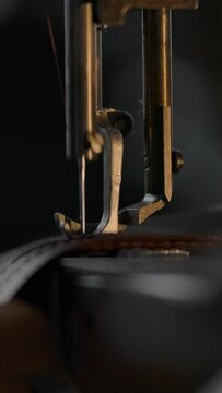 Close-up view of working sewing machine presser foot, stitching in slowmotion. Tailor's hand holding sewing leather carefully. Manufacturing handicraft unique individual bags, belts, accessories